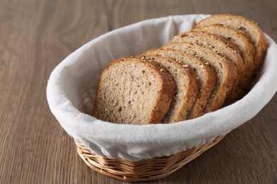 Photo of Fresh bread slices in wicker basket on wooden table, closeup