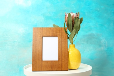 Photo of Blank frame and vase with flower on table near color wall. Mock up for design