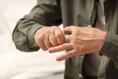 Senior man suffering from pain in hand on blurred background, closeup. Rheumatism symptom