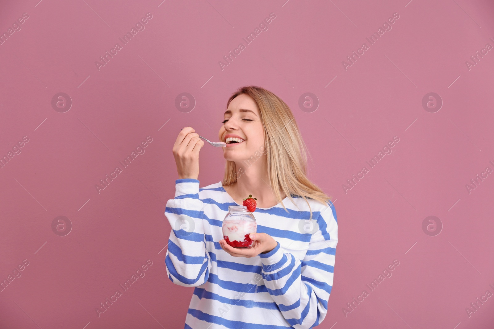 Photo of Young attractive woman eating tasty yogurt on color background