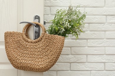 Photo of Stylish beach bag with beautiful wildflowers hanging on door handle. Space for text