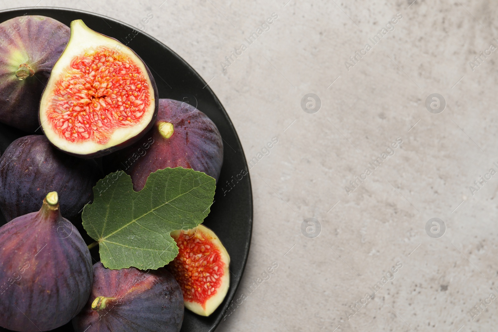 Photo of Whole and cut ripe figs with leaf on light grey textured table, top view. Space for text