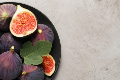 Whole and cut ripe figs with leaf on light grey textured table, top view. Space for text