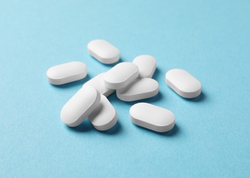 Photo of Many white pills on light blue background, closeup