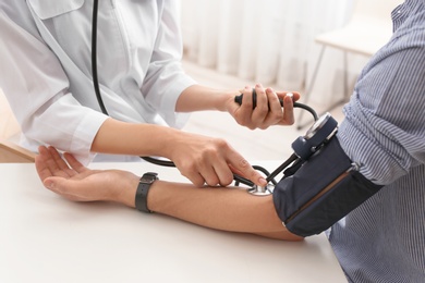 Photo of Doctor checking patient's blood pressure in hospital, closeup. Cardiology concept
