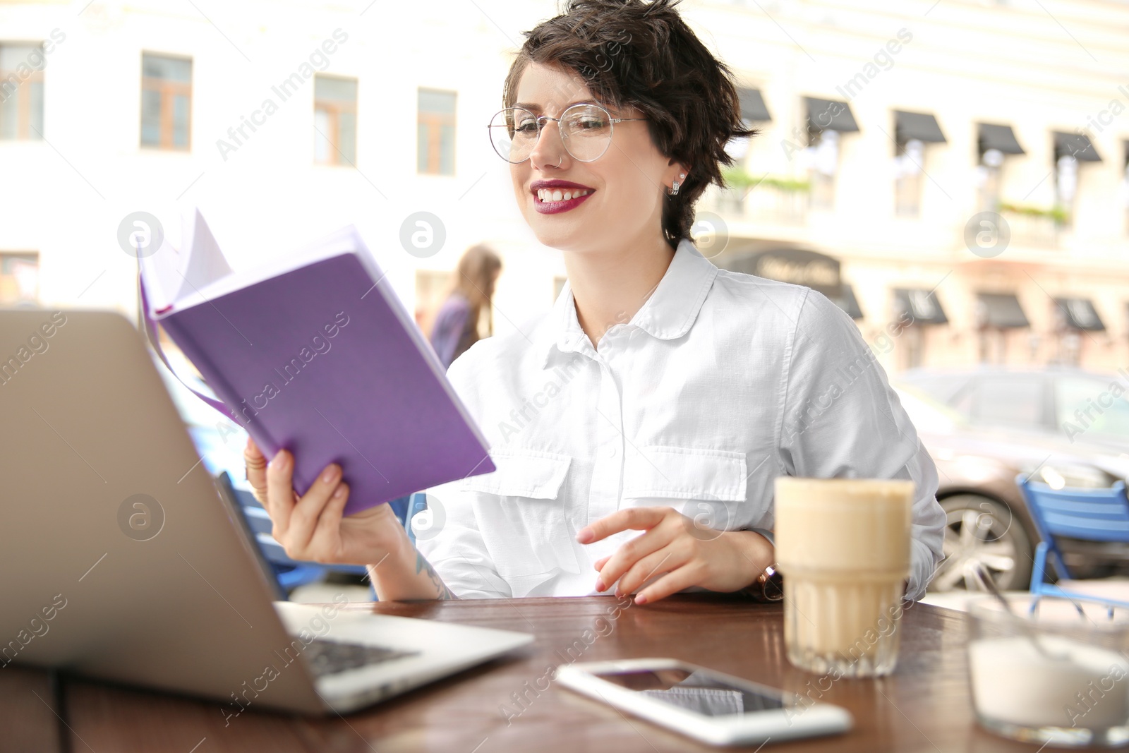 Photo of Young woman with notebook using laptop at desk in cafe