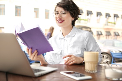 Young woman with notebook using laptop at desk in cafe
