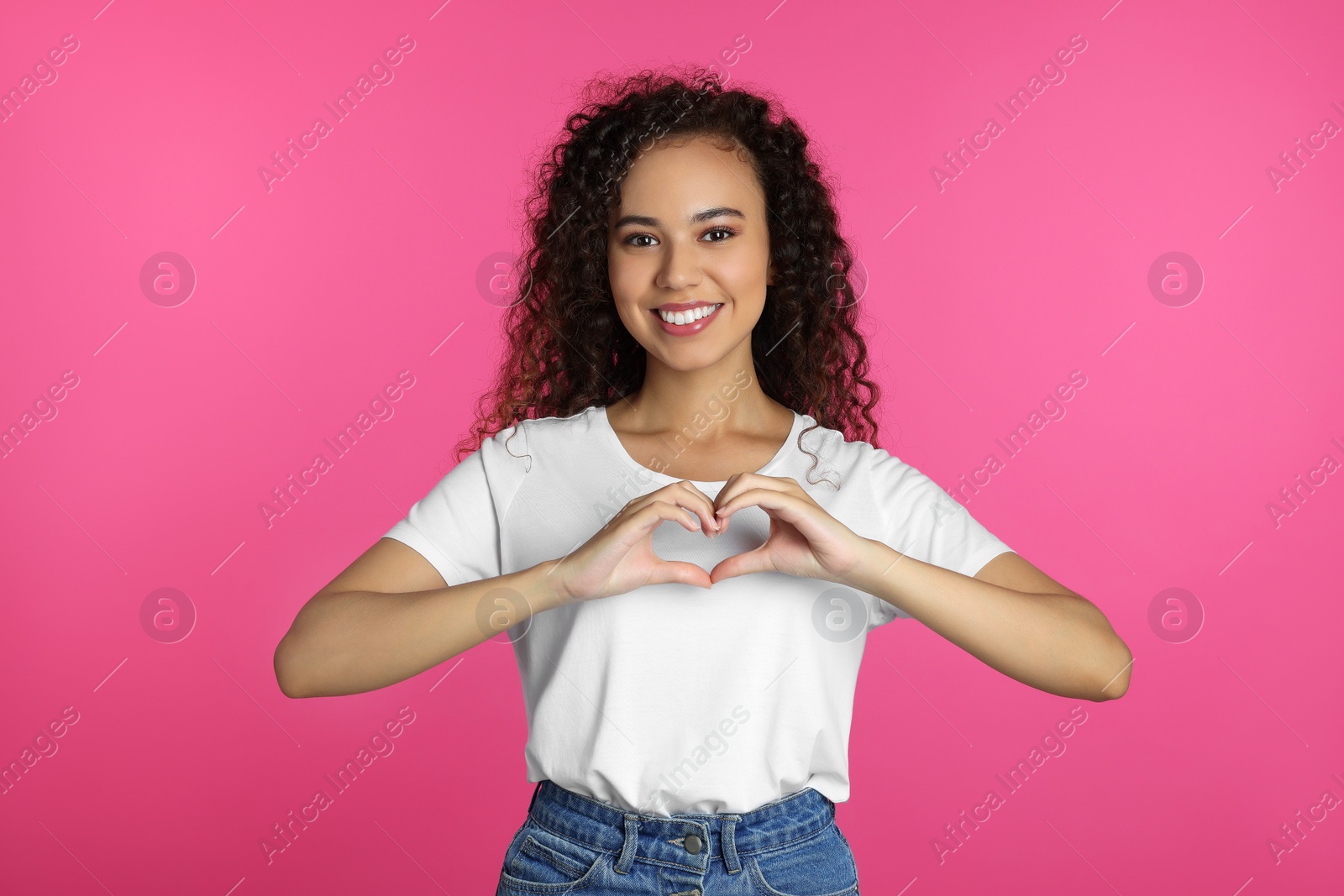 Photo of Happy young African-American woman making heart with hands on pink background