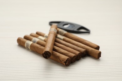 Cigars and guillotine cutter on white wooden table, closeup