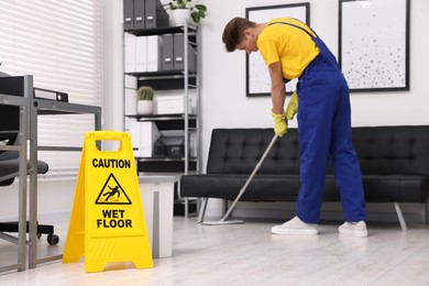 Photo of Cleaning service worker washing floor with mop. Wet floor sign in office