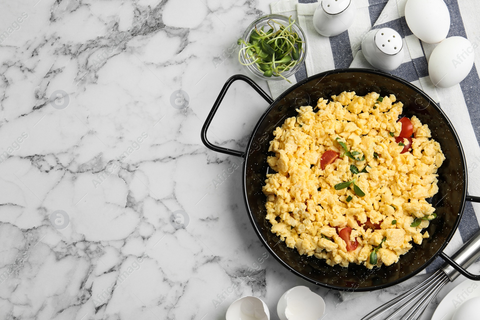 Photo of Tasty scrambled eggs with sprouts and cherry tomato in wok pan on white marble table, flat lay. Space for text