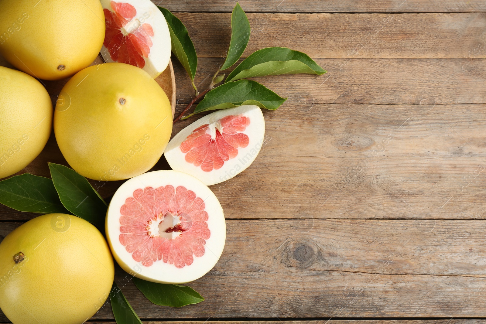 Photo of Fresh cut and whole pomelo fruits on wooden table, flat lay. Space for text