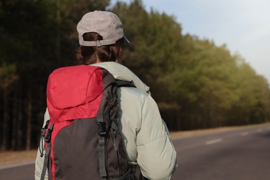 Young woman with backpack on road near forest, back view