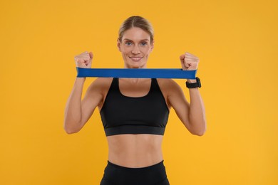 Photo of Woman exercising with elastic resistance band on orange background