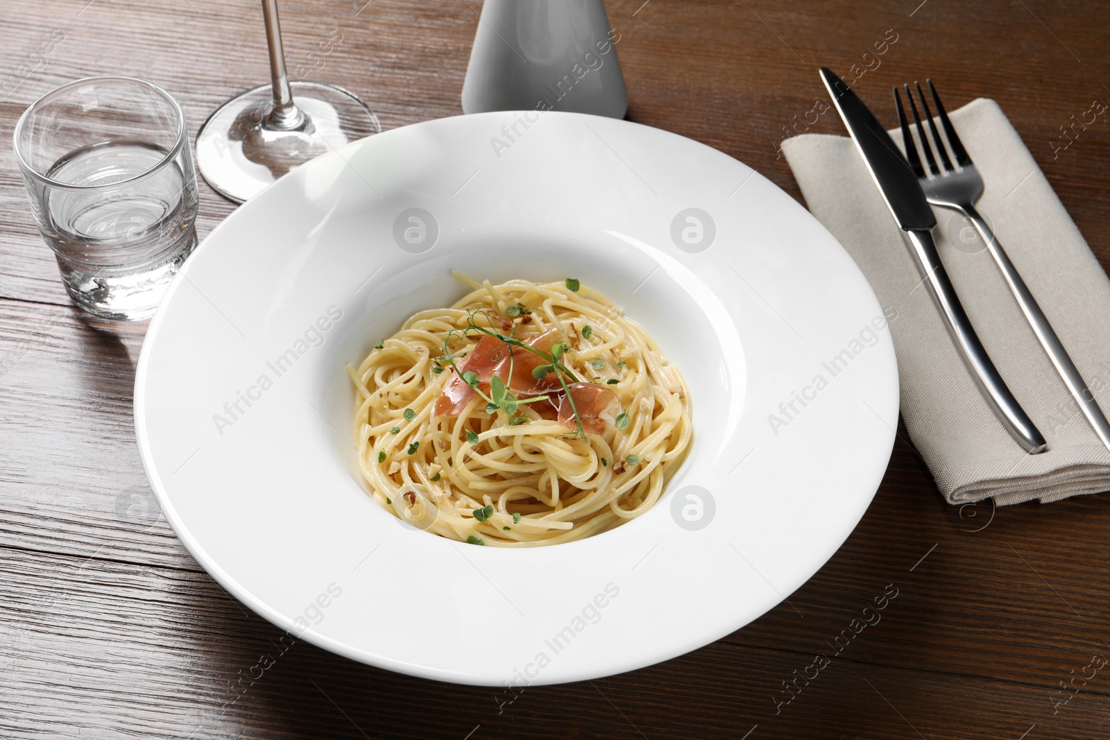 Photo of Tasty spaghetti with prosciutto and microgreens served on wooden table. Exquisite presentation of pasta dish