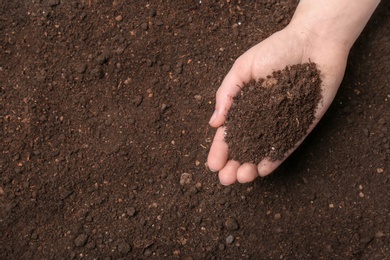 Woman holding pile of soil above ground, top view. Space for text