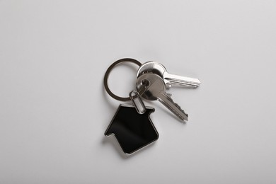 Keys with trinket in shape of house on white background, top view. Real estate agent services