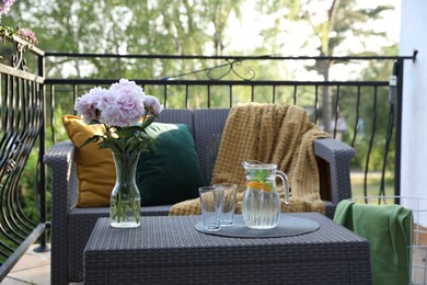 Photo of Rattan table with jug of water, glasses and beautiful flowers on terrace