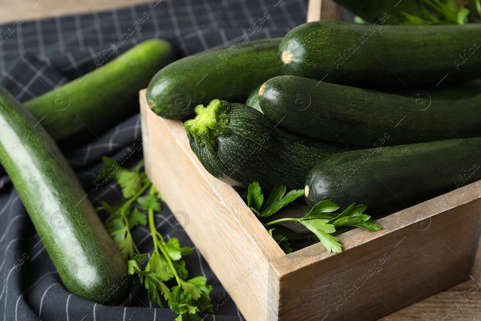 Photo of Crate with green zucchinis and parsley on table, closeup