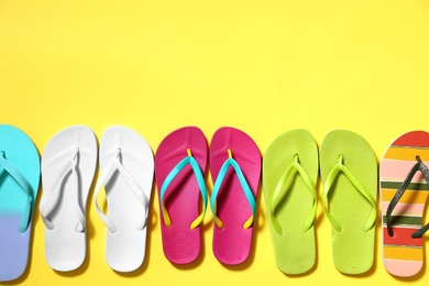 Photo of Different flip flops and space for text on yellow background, flat lay. Summer beach accessories