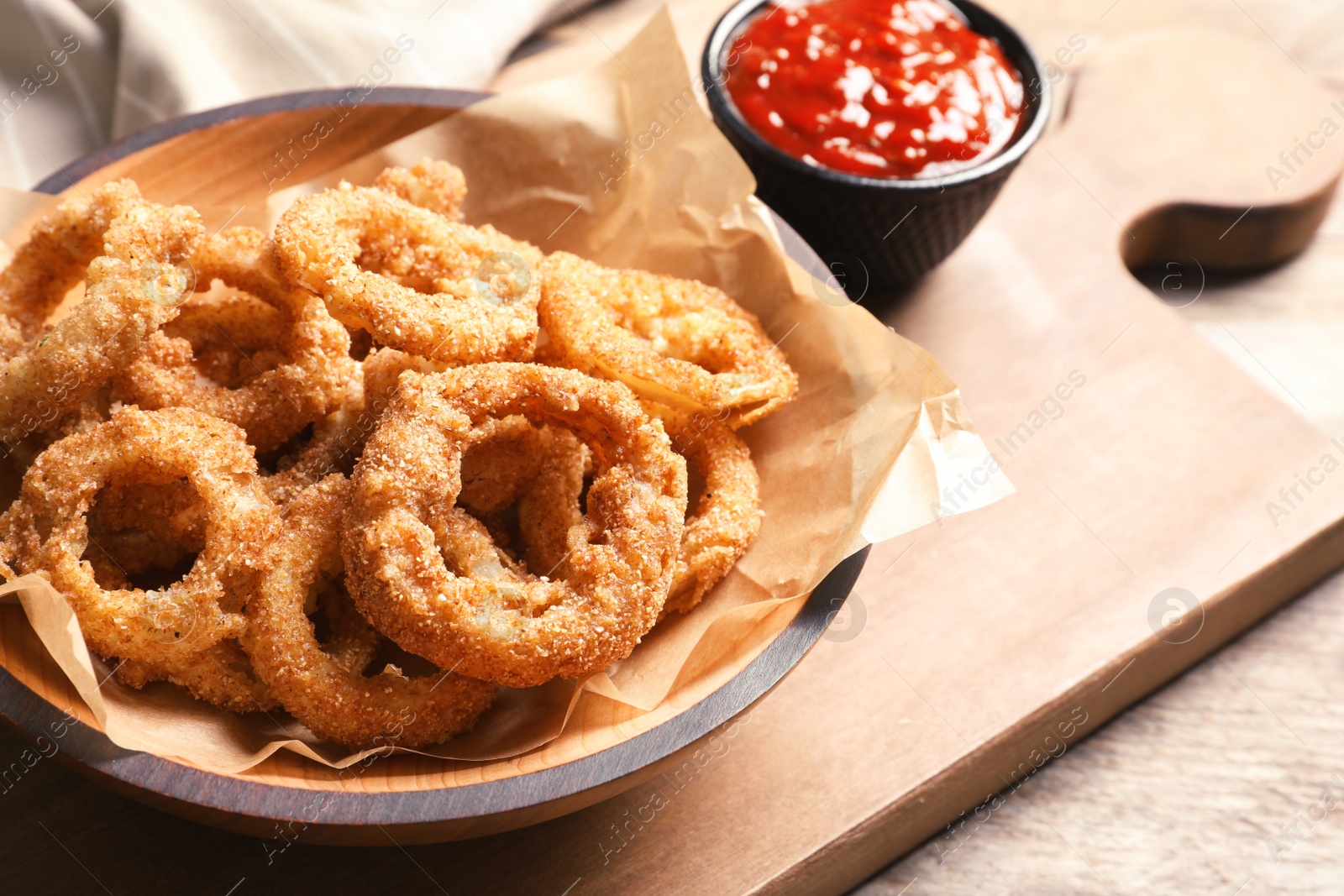 Photo of Homemade crunchy fried onion rings in plate and sauce on wooden background, closeup