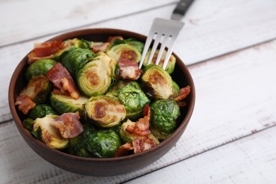 Photo of Delicious roasted Brussels sprouts and bacon in bowl on light wooden table, closeup