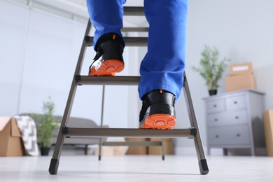 Photo of Professional worker climbing up ladder in room, closeup
