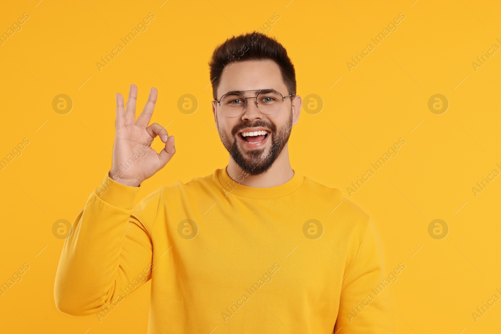 Photo of Handsome man in glasses showing OK gesture on orange background