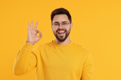 Photo of Handsome man in glasses showing OK gesture on orange background