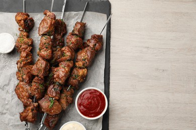 Metal skewers with delicious meat, ketchup and sauce served on white wooden table, top view. Space for text