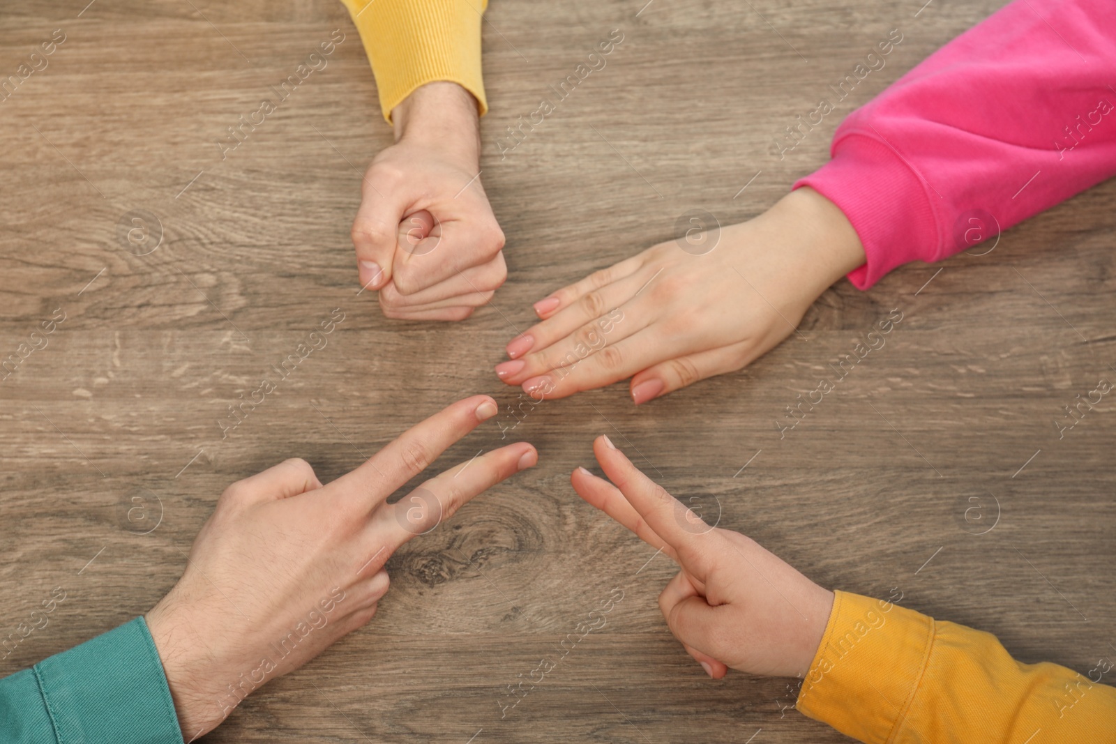 Photo of Closeup of people playing rock, paper and scissors on wooden background, top view