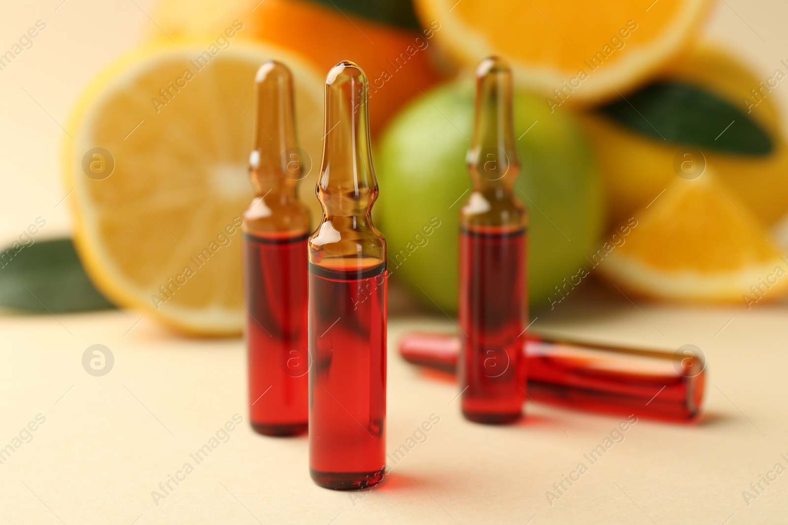 Photo of Skincare ampoules with vitamin C, different citrus fruits and leaves on beige background, closeup