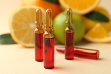 Skincare ampoules with vitamin C, different citrus fruits and leaves on beige background, closeup