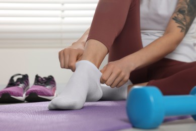 Woman putting on white socks on exercise mat indoors, closeup