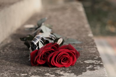 Photo of Red roses on grey tombstone outdoors, space for text. Funeral ceremony