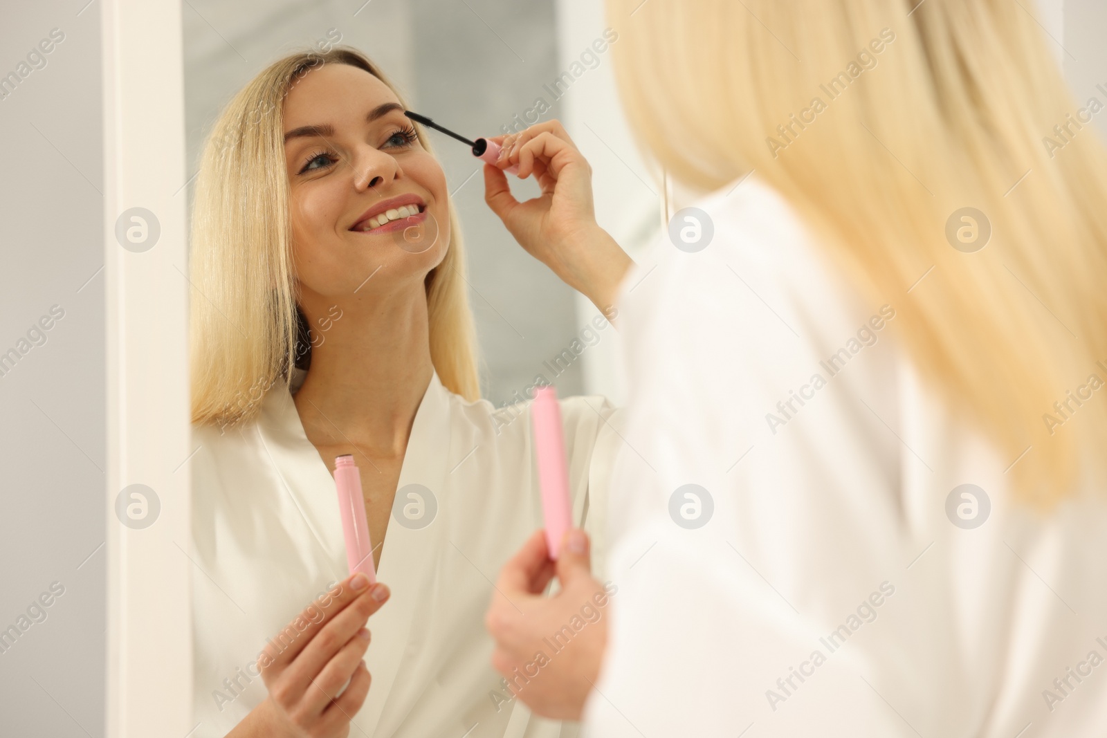 Photo of Beautiful woman applying mascara near mirror in bathroom