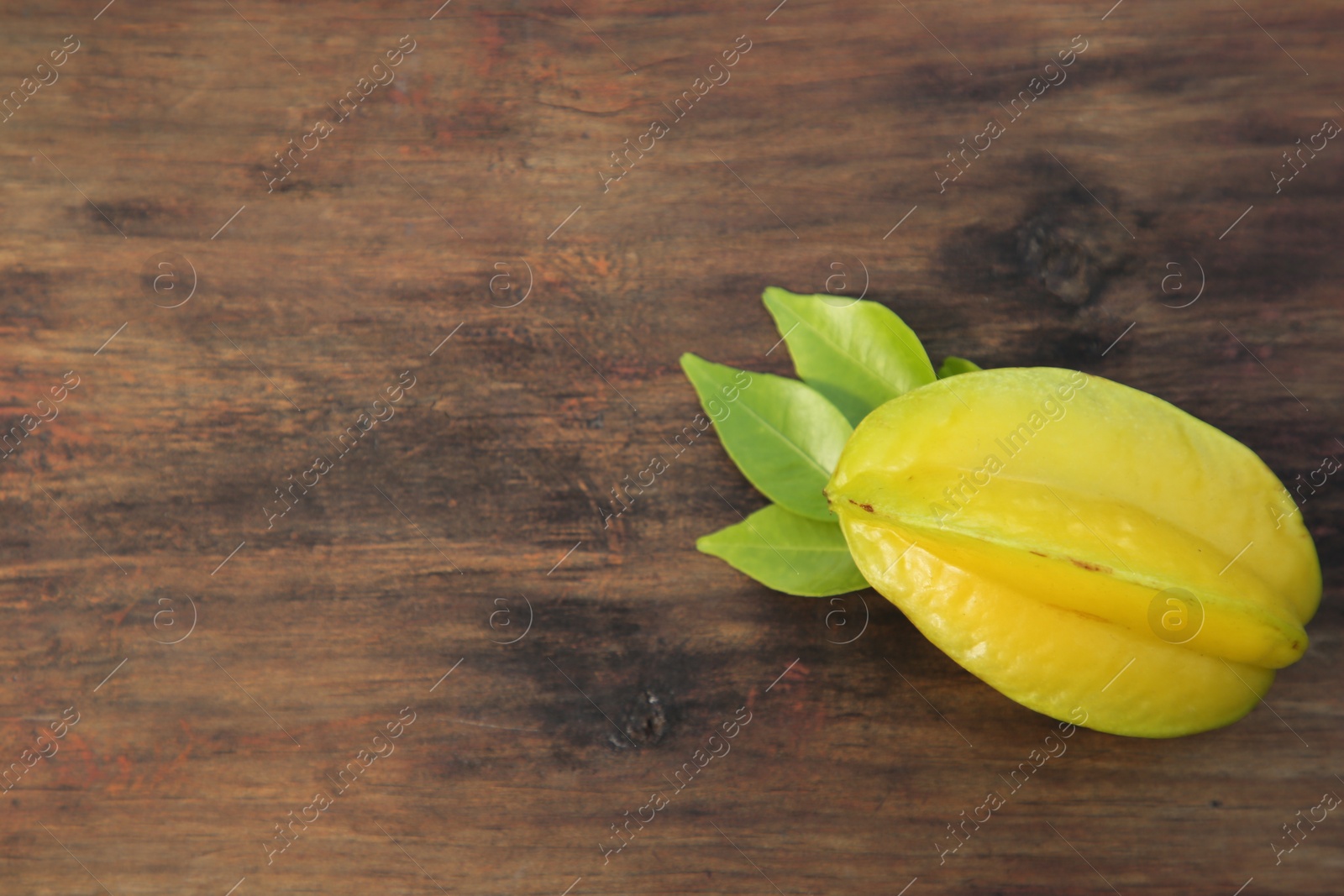 Photo of Delicious ripe carambola with leaves on wooden table, top view. Space for text