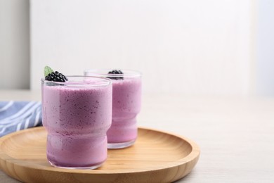 Delicious blackberry smoothie in glasses on white wooden table. Space for text