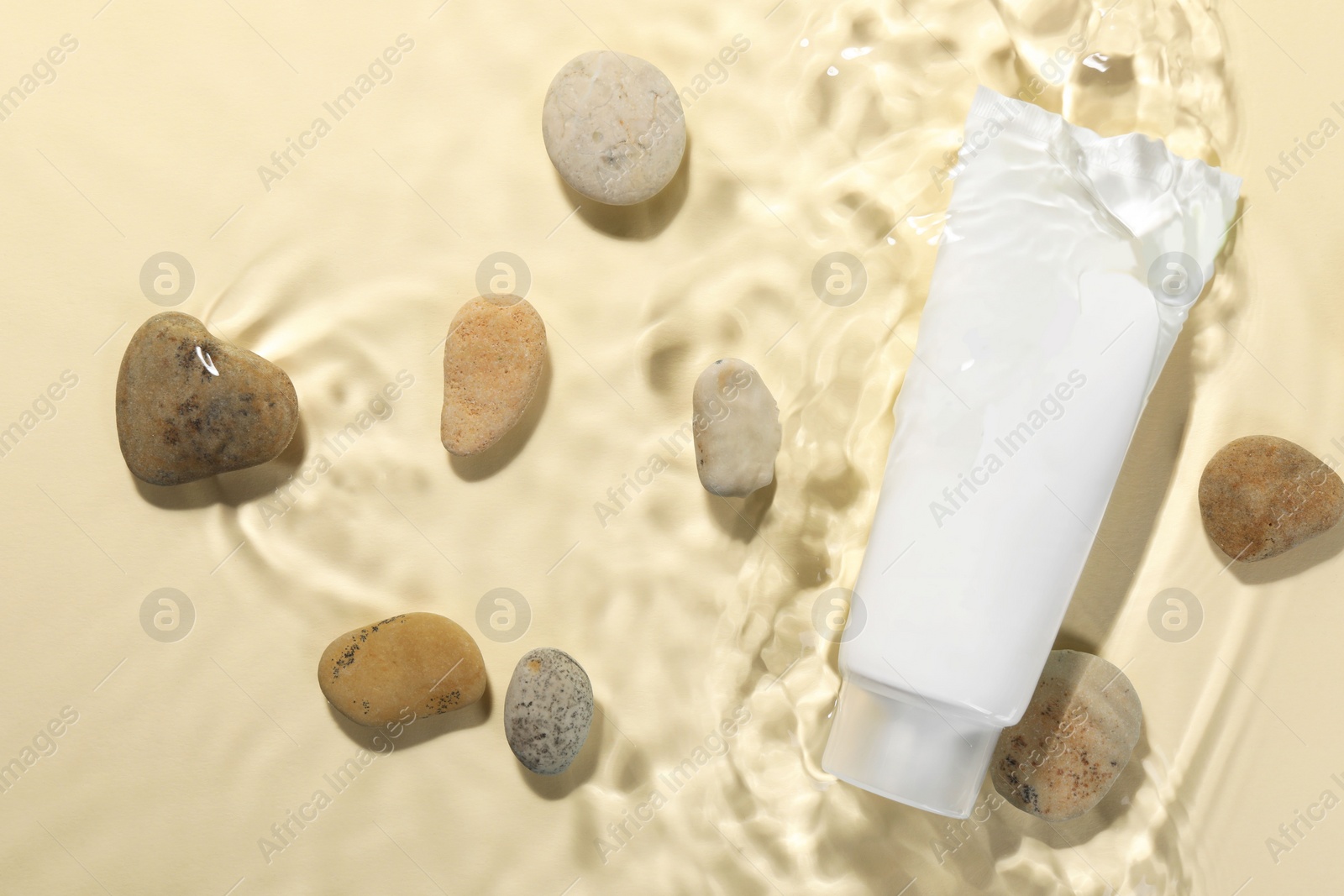 Photo of Tube of face cleansing product and stones in water against beige background, flat lay