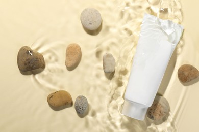 Tube of face cleansing product and stones in water against beige background, flat lay