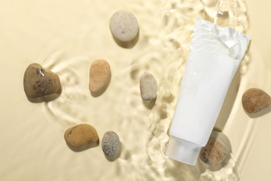 Photo of Tube of face cleansing product and stones in water against beige background, flat lay