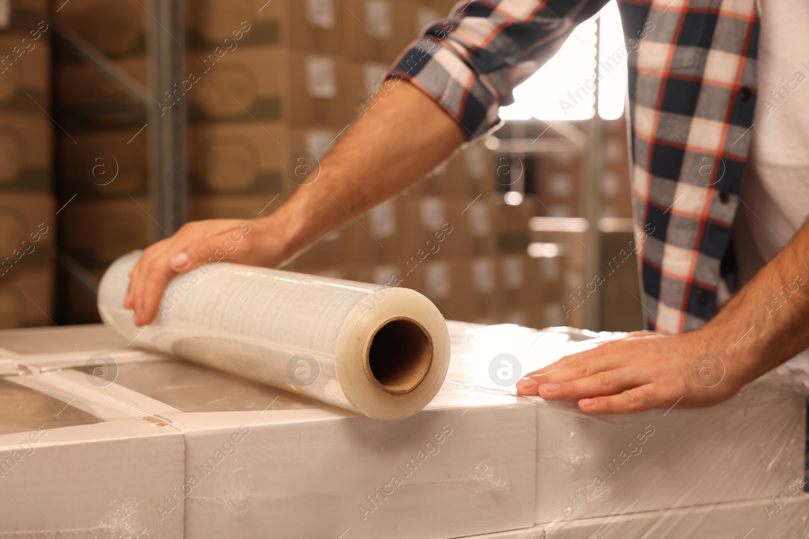 Photo of Worker wrapping boxes in stretch film at warehouse, closeup