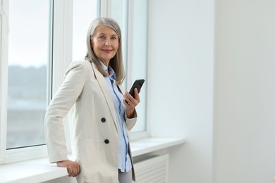 Senior woman using mobile phone at home, space for text