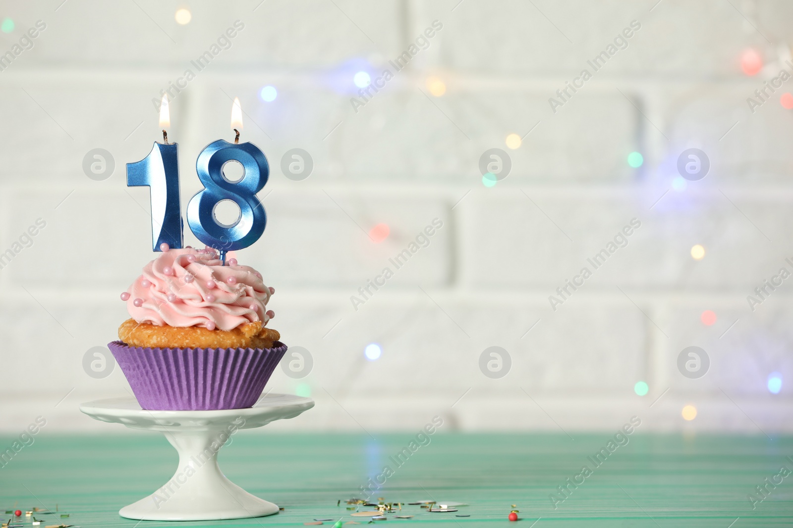 Photo of 18th birthday, coming of age party. Delicious cupcake with number shaped candles on turquoise table, space for text