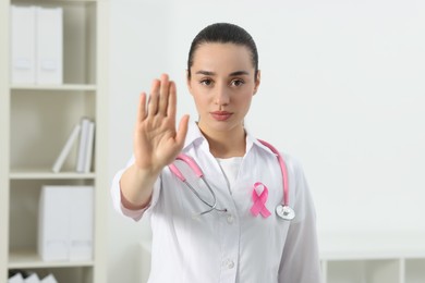 Photo of Mammologist with pink ribbon showing stop gesture in hospital. Breast cancer awareness