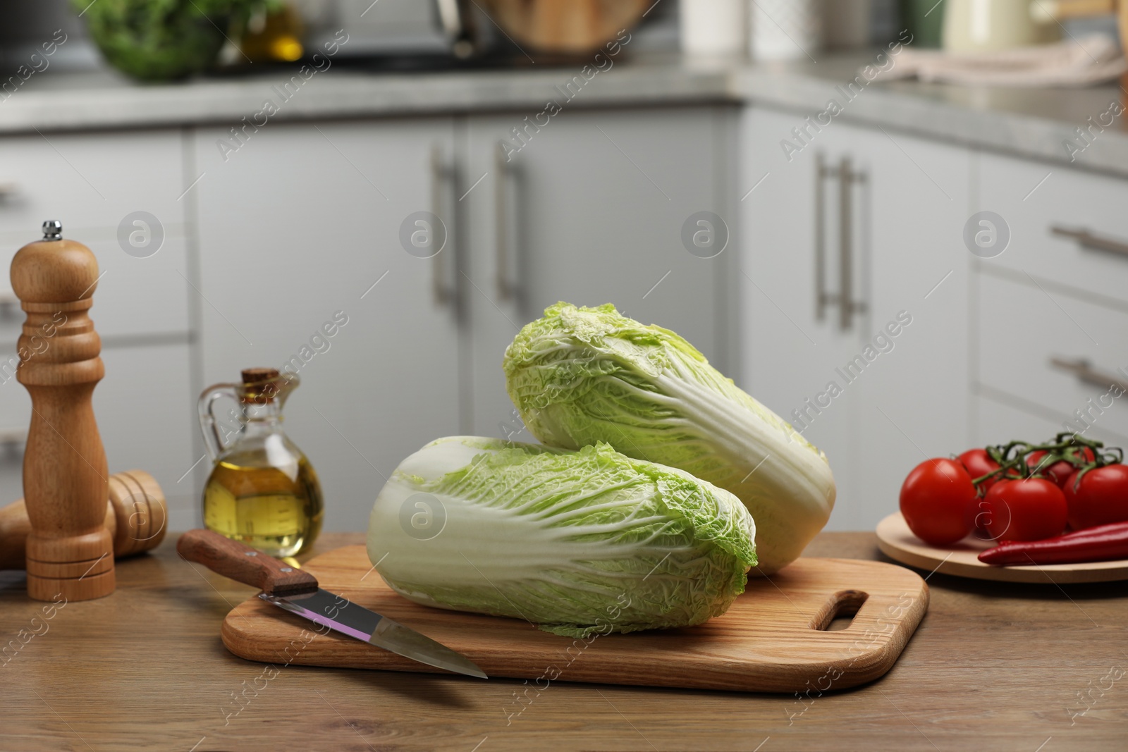 Photo of Fresh Chinese cabbages, knife, tomatoes and oil on wooden table in kitchen