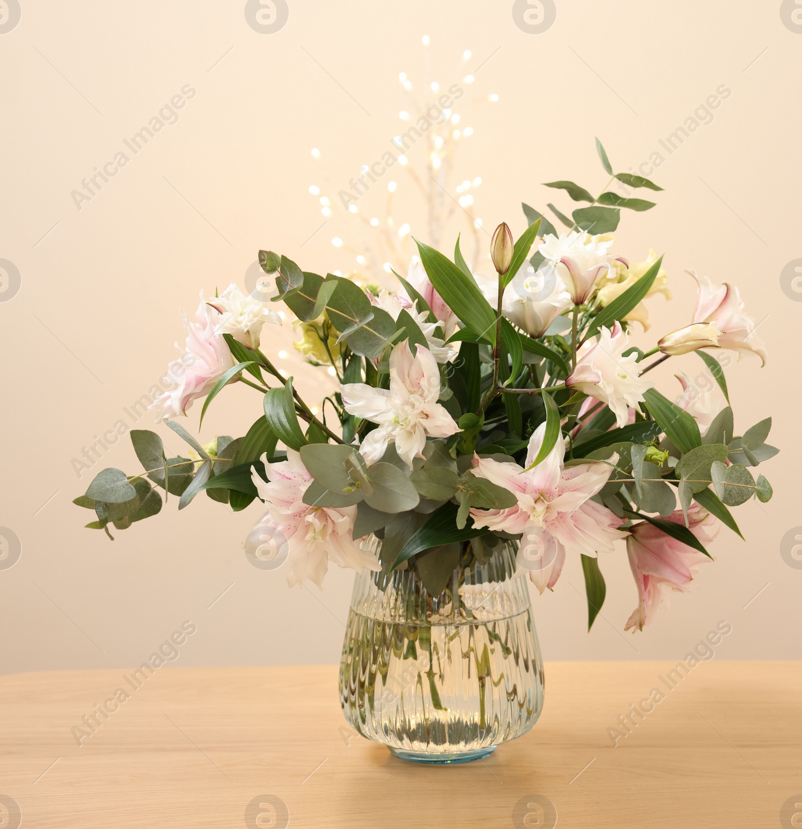 Photo of Bouquet of beautiful lily flowers in vase on wooden table against beige background