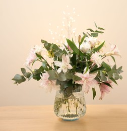 Photo of Bouquet of beautiful lily flowers in vase on wooden table against beige background