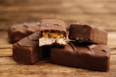 Photo of Chocolate bars with caramel, nuts and nougat on wooden table, closeup