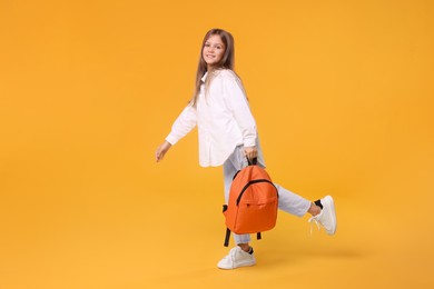 Photo of Happy schoolgirl with backpack on orange background